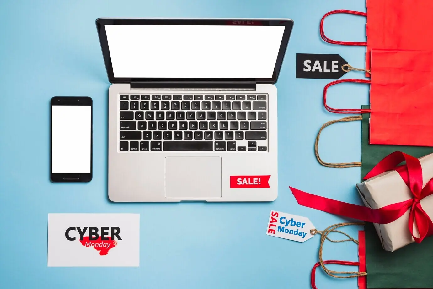 Ноутбук расположен рядом со смартфоном, бирками, подарком и пакетами.